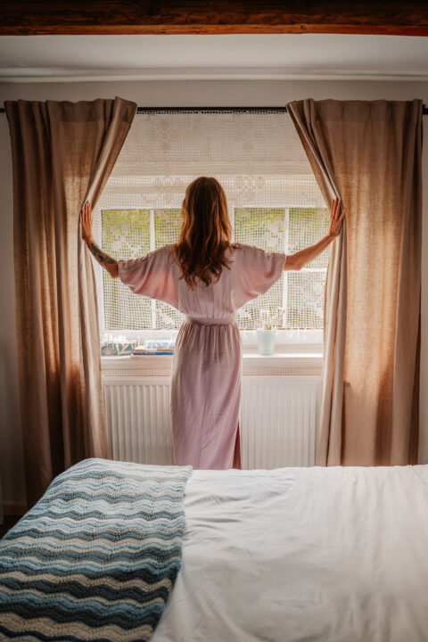 Kobieta otwiera zasłony przy oknie, widok wnętrza.