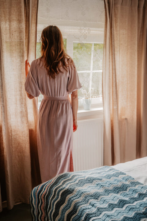 Osoba patrzy przez okno zasłonięte zasłonami.