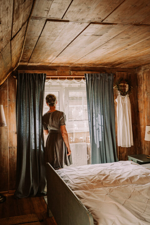 Kobieta stoi przy oknie w drewnianym pokoju.