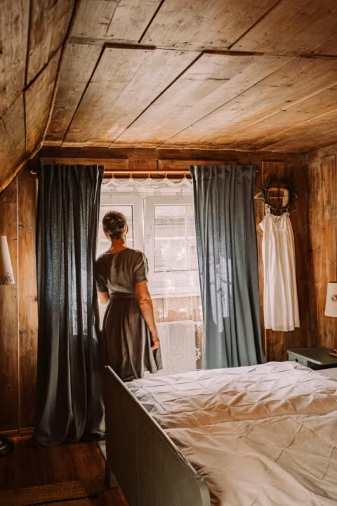 Kobieta stoi przy oknie w drewnianym pokoju.