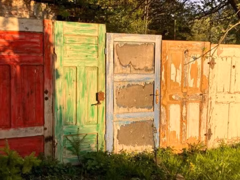 Stare, kolorowe drzwi w ogrodzie o zachodzie słońca.